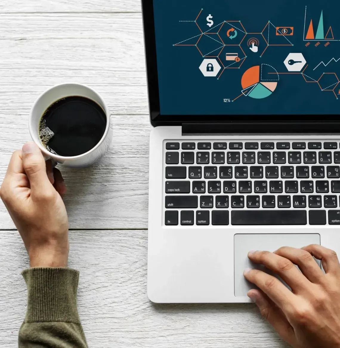 Hand holding a coffee mug beside a laptop with analytics graphics on screen, another hand on the trackpad.