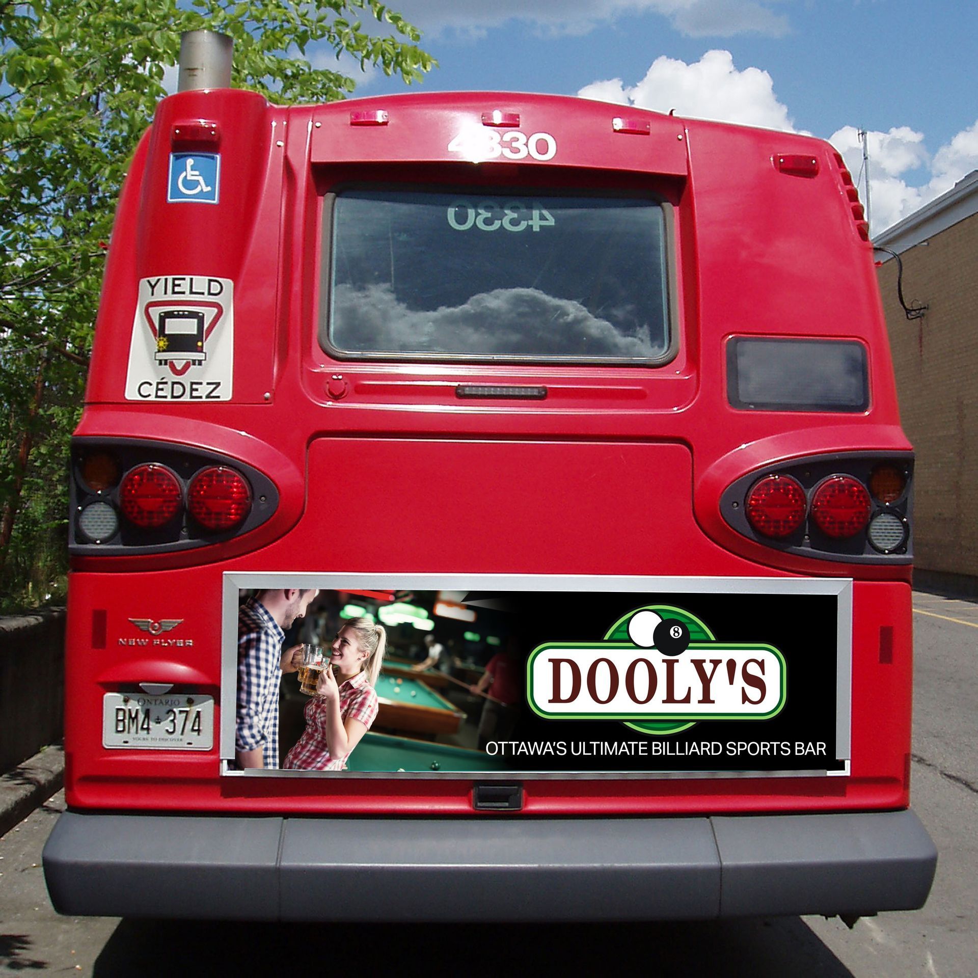 Rear view of a red city bus with accessibility signs and a DOOLY’S ad on the back.