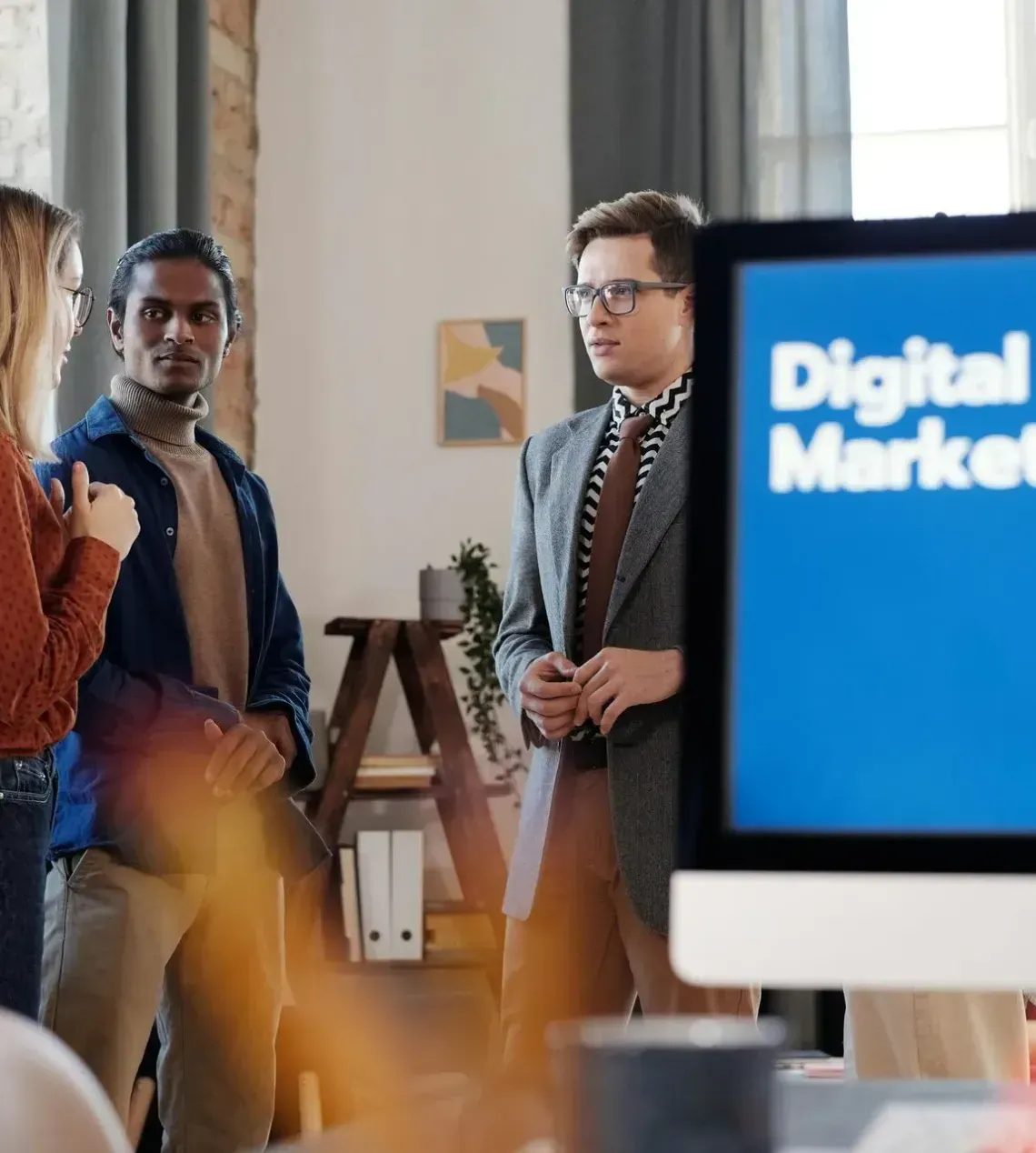 Three coworkers talking in an office beside a screen reading “Digital Marketing”