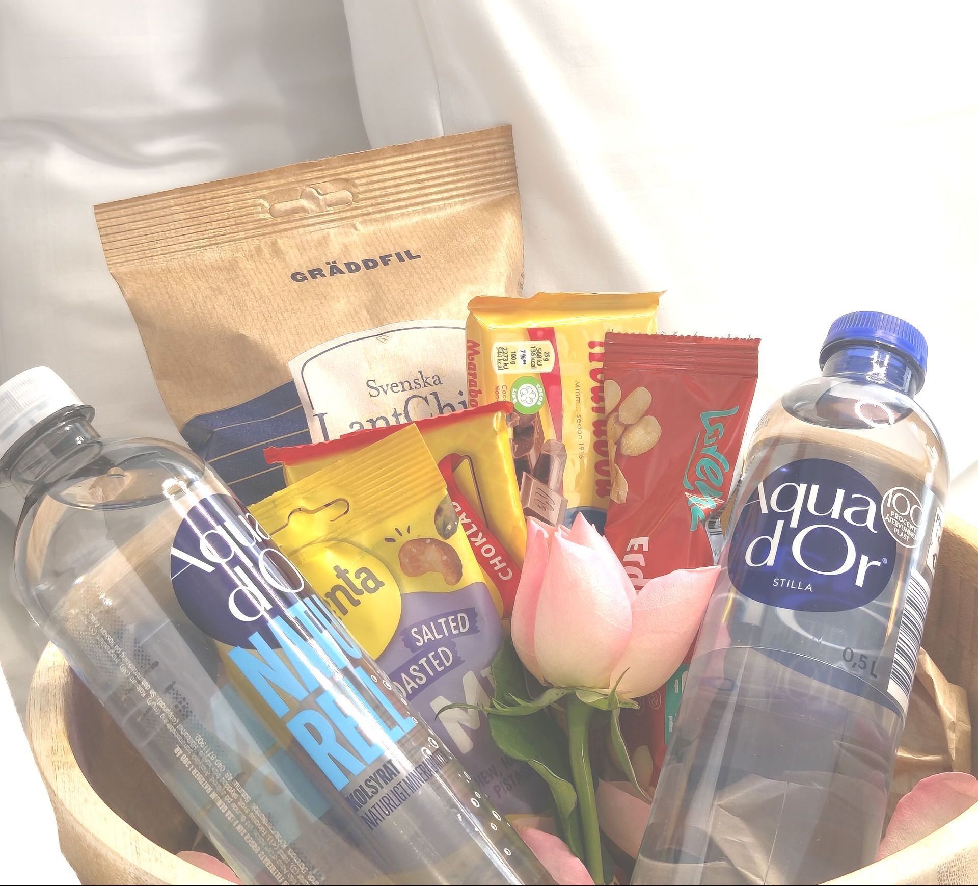 Gift basket with bottled water, snacks, and pink flowers on a white background