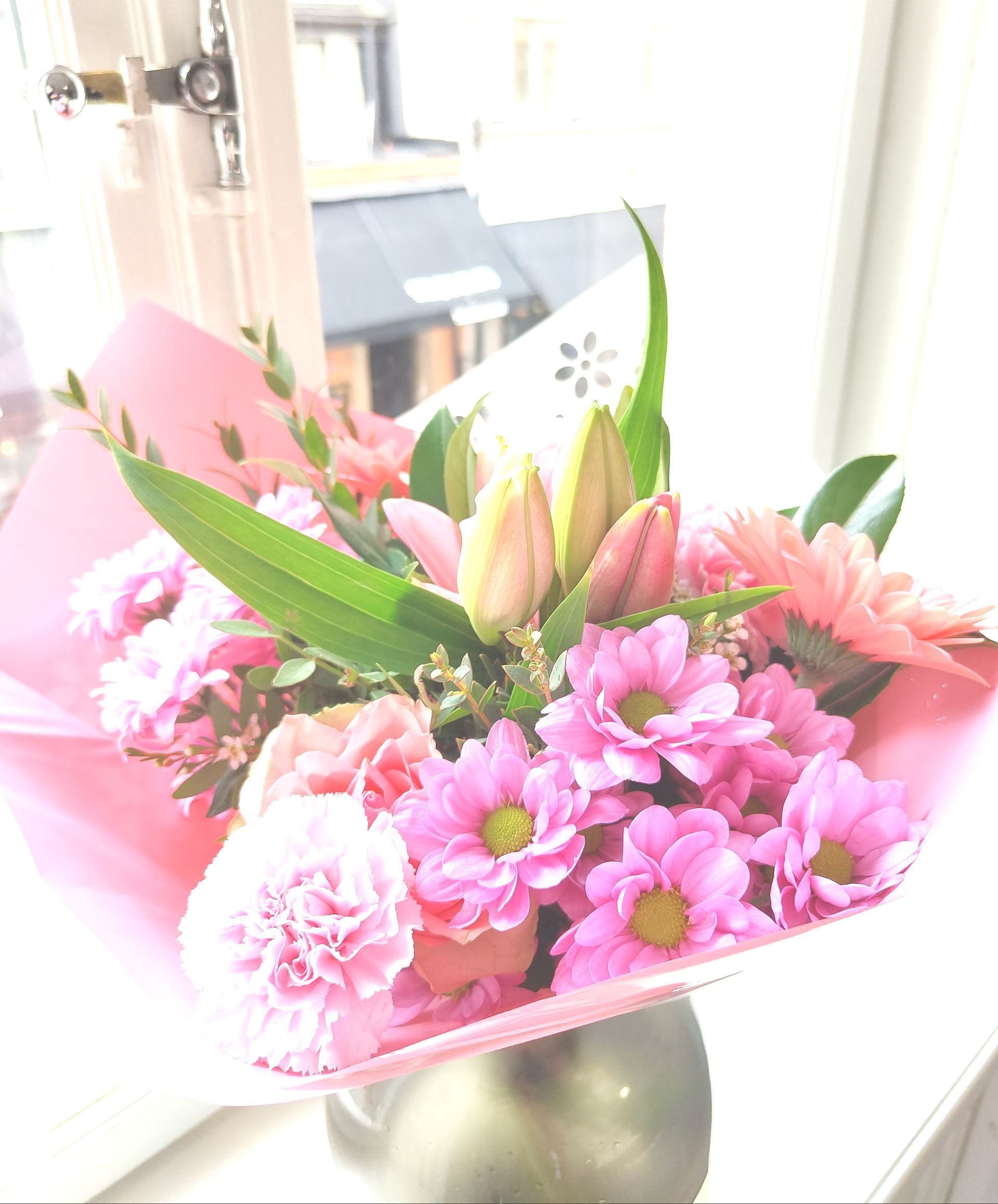 Pink and white flower bouquet in pink wrapping on a table near a window