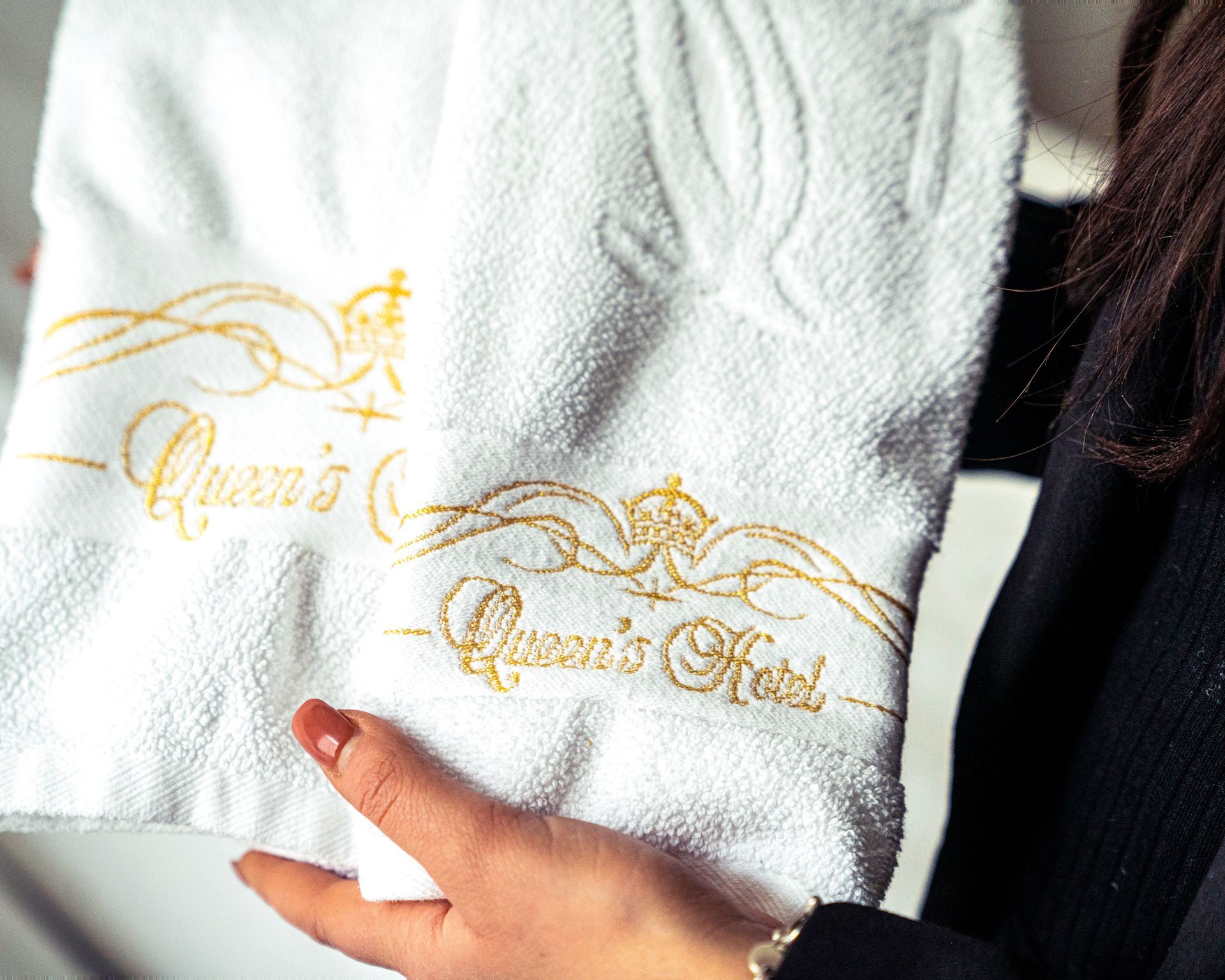 White embroidered towels with gold lettering, held by a hand in a dark sleeve