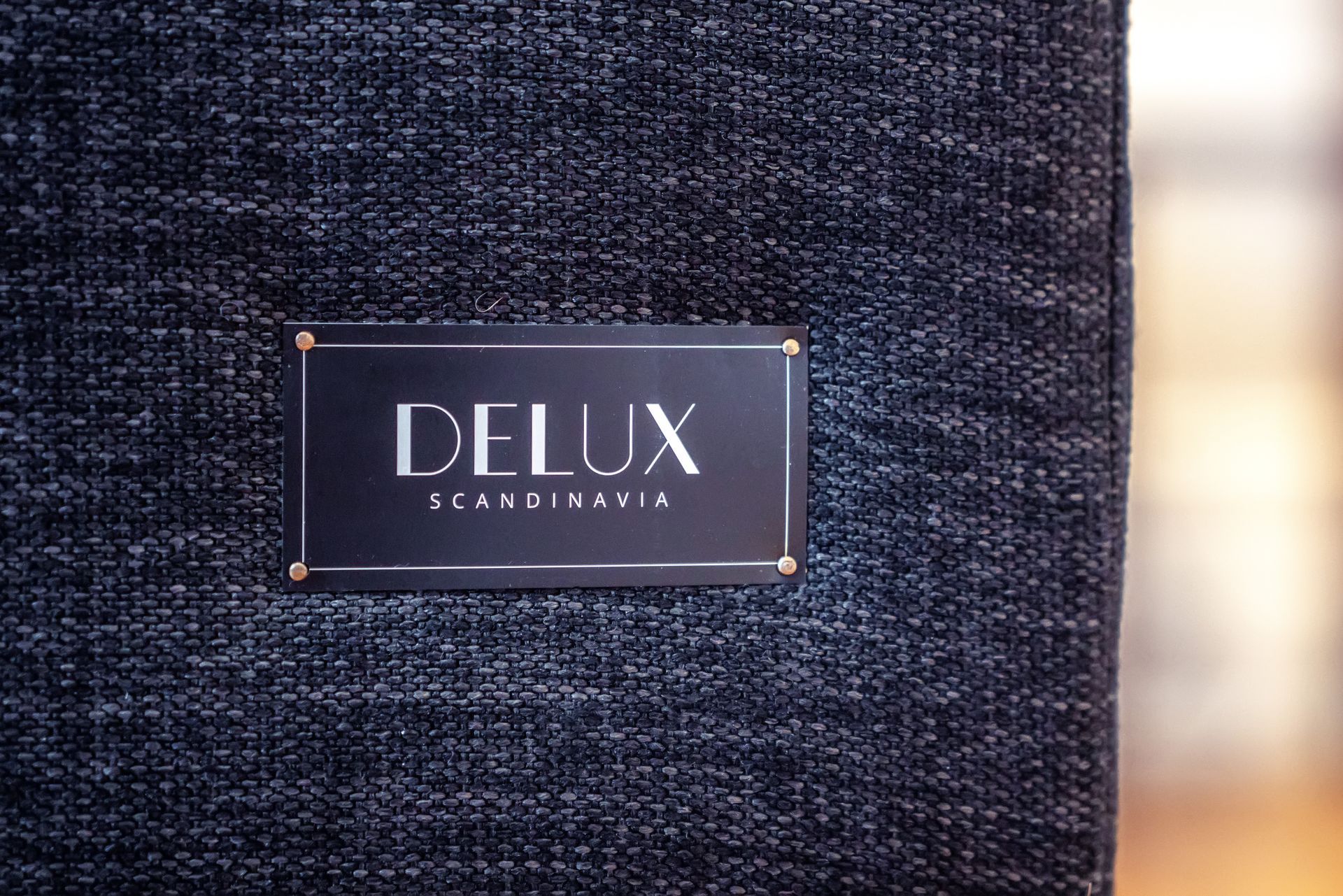 Close-up of a dark fabric sign with a metal plaque reading “DELUX” and smaller text below.