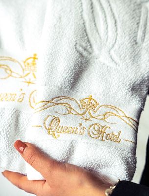 White towel with gold “Queen’s Hall” embroidery held by a hand.