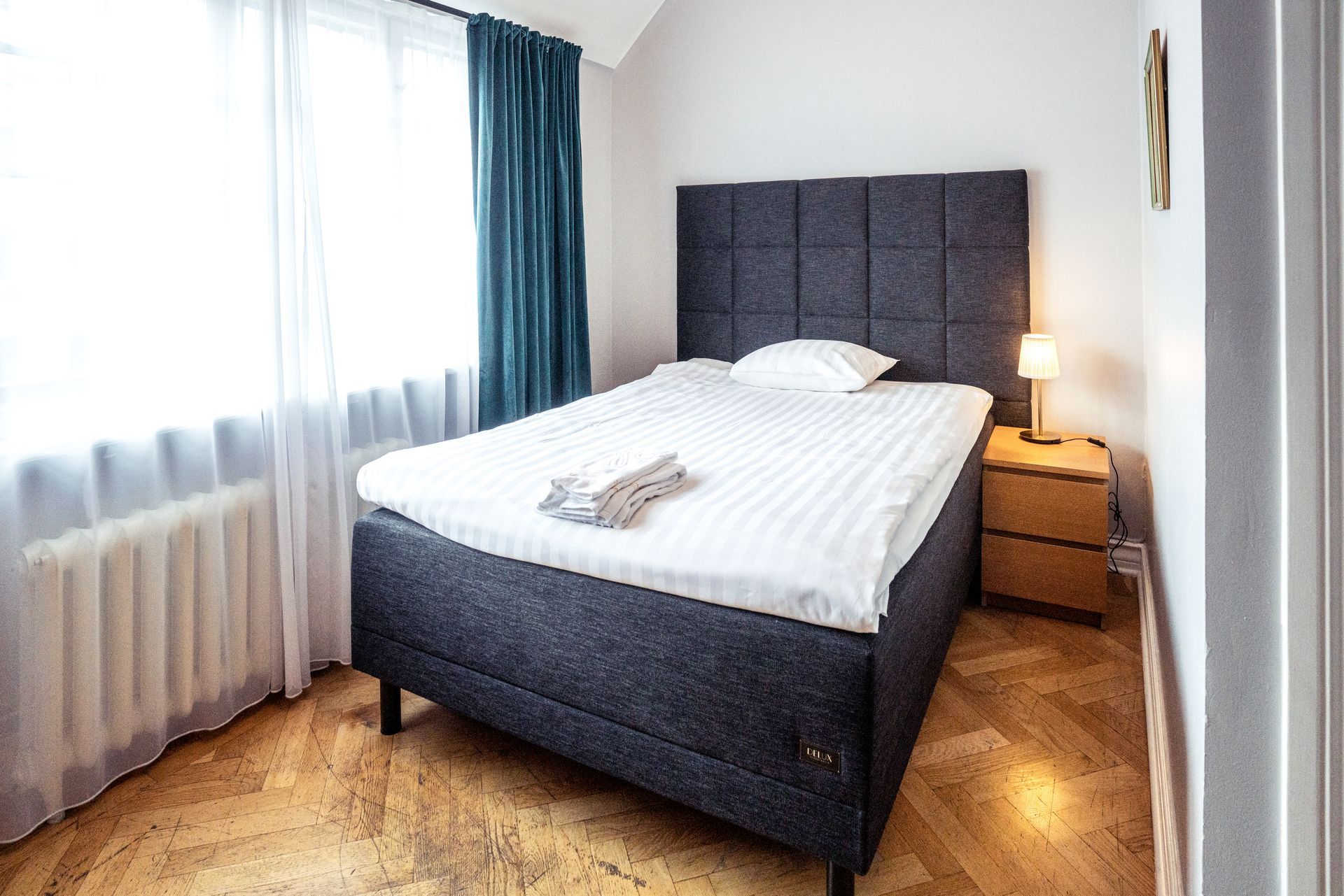 Modern bedroom with gray upholstered bed, white bedding, bedside lamp, and large window with sheer curtains