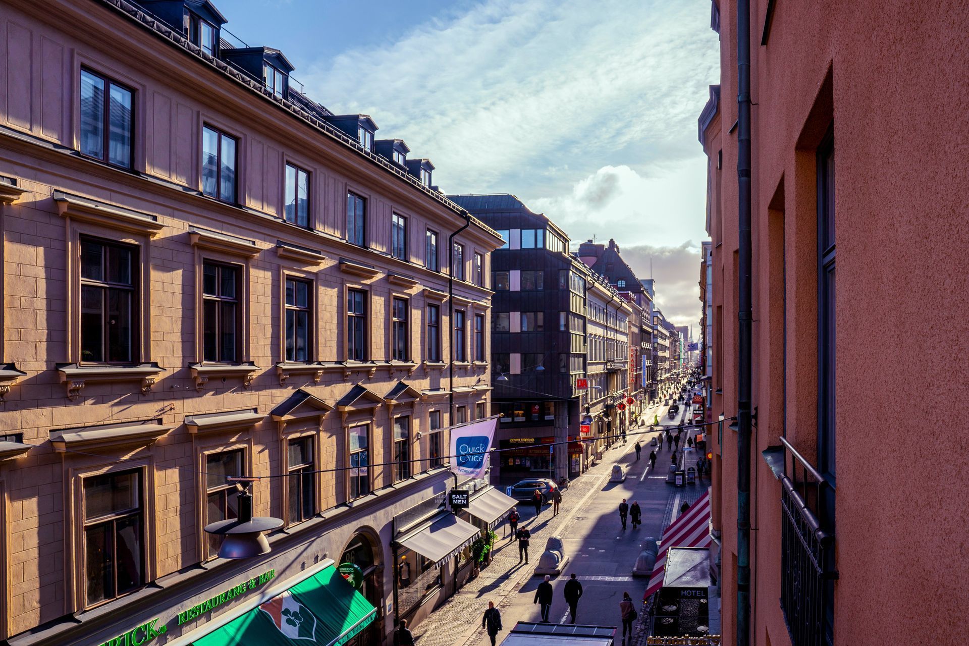 City street view with historic buildings, pedestrians, and a bright blue sky