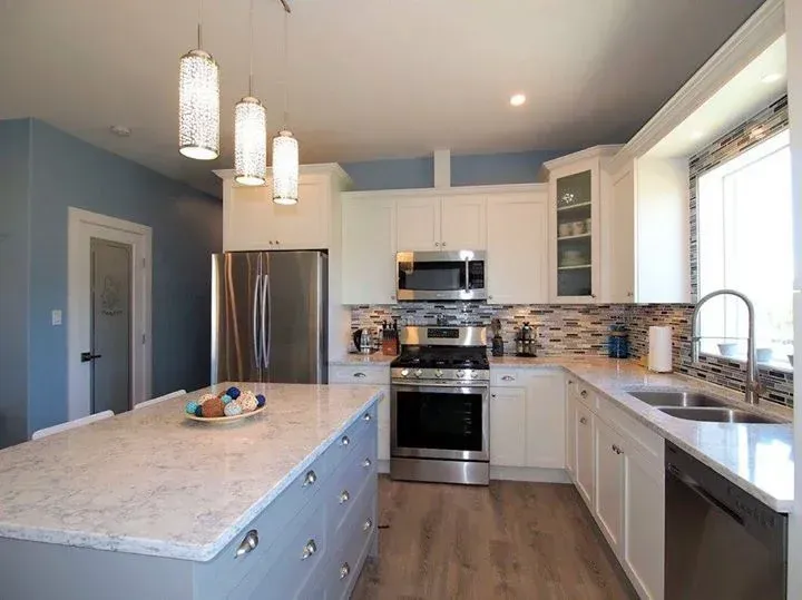 Modern kitchen with white cabinets, stainless steel appliances, blue walls, and a large island.