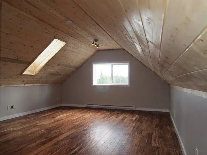 Attic room with wood floor and ceiling, skylight, and window. Walls are painted gray.