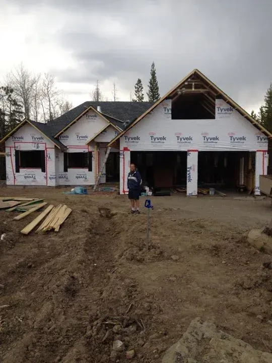 House under construction, covered in Tyvek wrap, with garage doors open. Person stands in front.