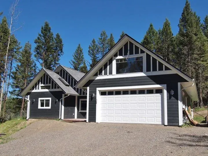 Dark gray house with white trim and a white garage door, set against a backdrop of trees and a bright blue sky.