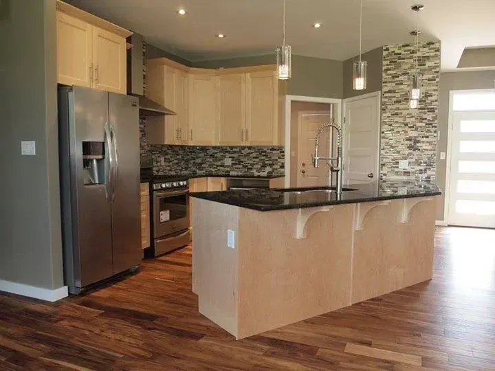 Modern kitchen with light wood cabinets, stainless steel appliances, dark countertops, and a central island.