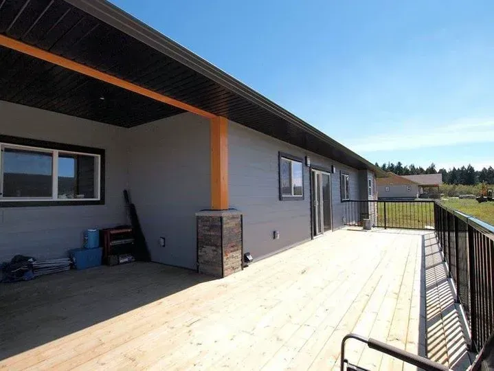 A modern home with a wooden deck and a black railing under a blue sky.