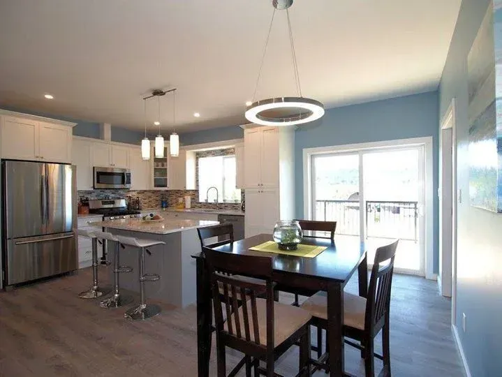 Modern kitchen and dining area with white cabinets, stainless steel appliances, and a square table.