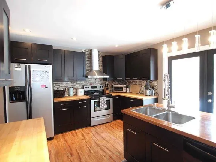Modern kitchen with black cabinets, stainless steel appliances, wood countertops, and a tile backsplash.