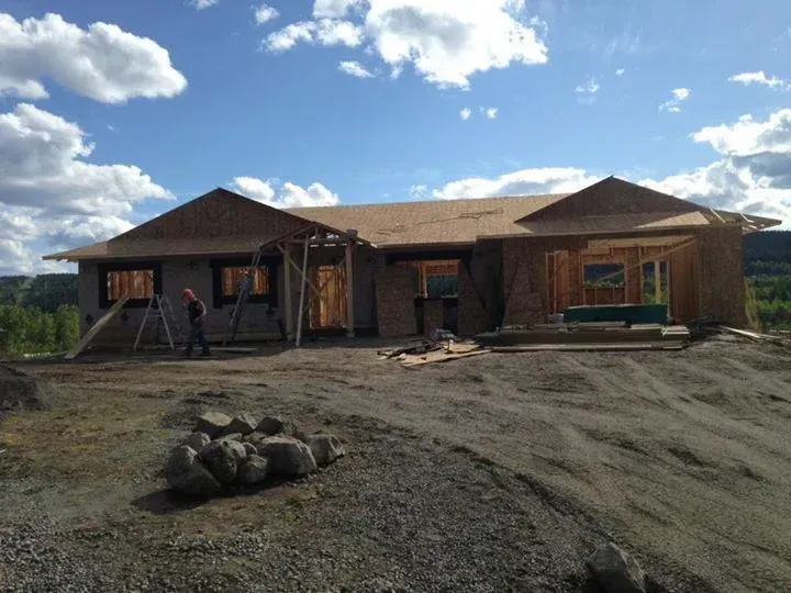 House under construction on a gravel hill under a cloudy sky; a worker stands in front.