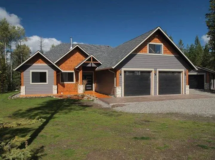 A modern house with gray siding, a wood facade, and a two-car garage under a bright blue sky.