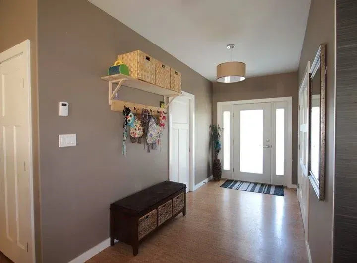 Hallway with brown walls, wooden bench with baskets, coats hanging, and double glass doors.