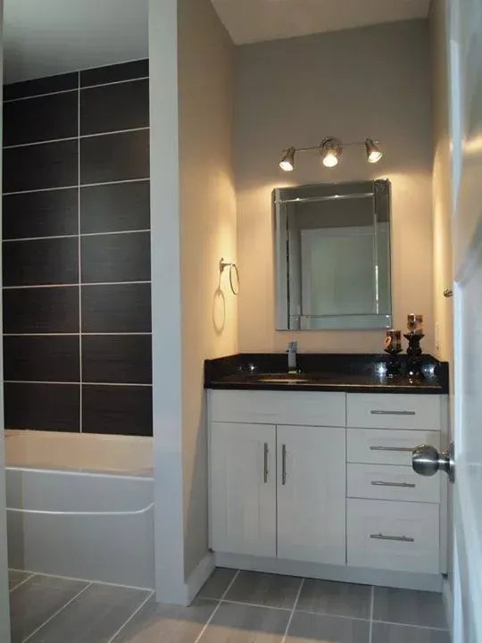 Modern bathroom with black tiled shower wall, white vanity, and gray floor tiles.
