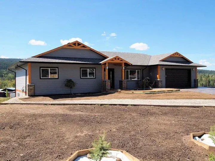 Gray house with wooden accents, blue sky background. Driveway and unplanted yard in front.