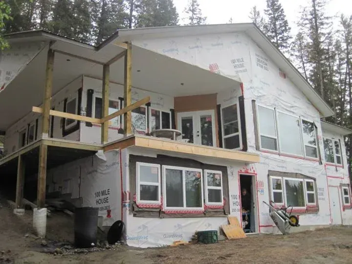 Two-story house under construction, wrapped in white material. Balcony and windows are visible.