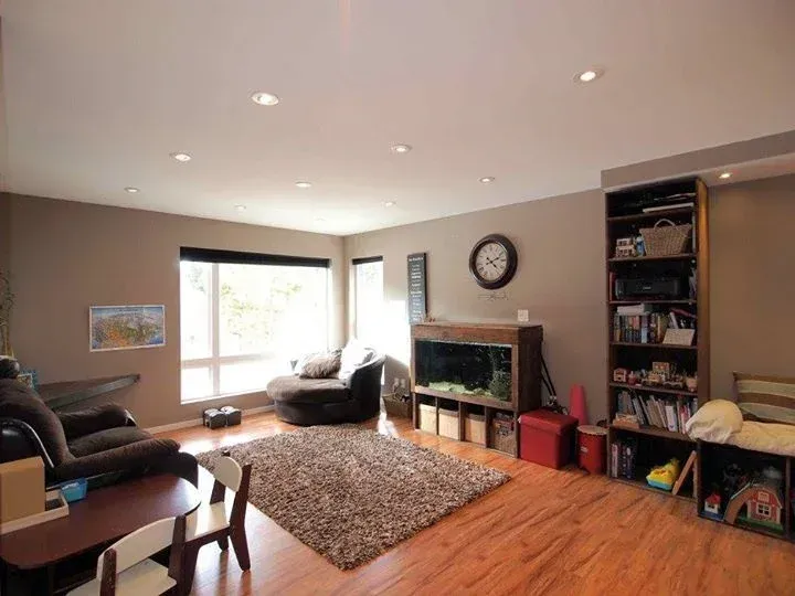 Living room with brown walls, wood floor, round rug, sofa, aquarium, bookshelf, and large window.