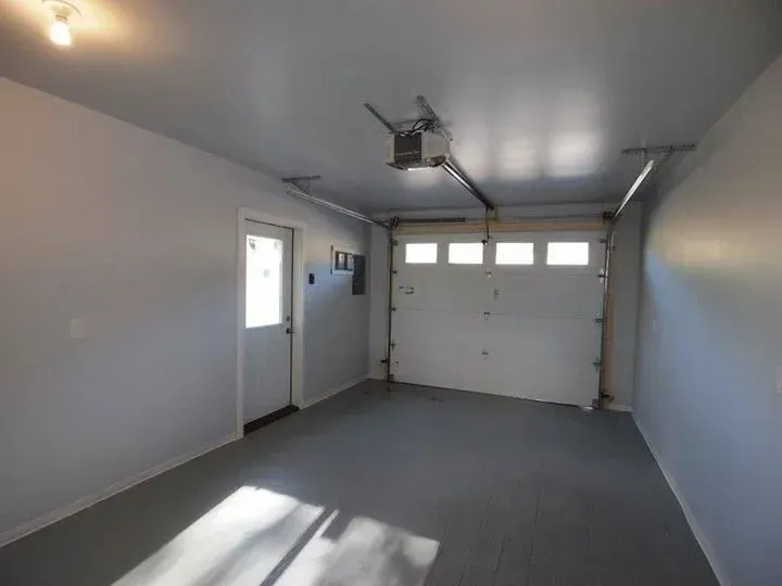 Empty garage interior with a gray floor and white walls, door, and garage door.