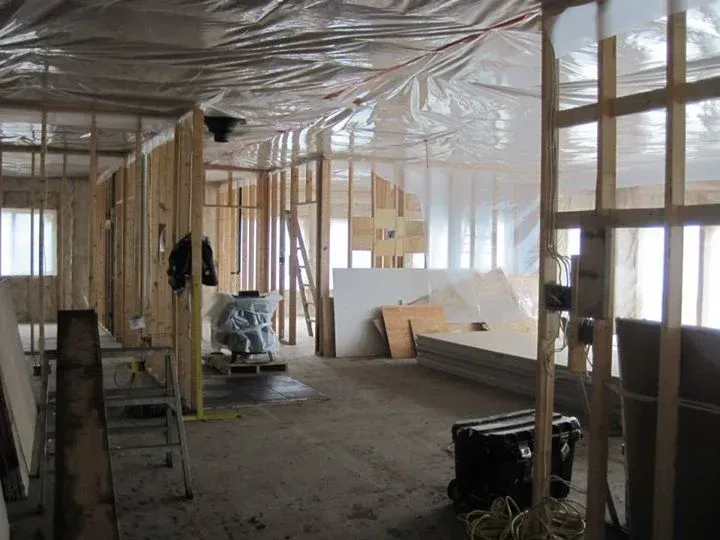 Interior of a building under construction, wooden frames, plastic sheeting, and materials scattered.