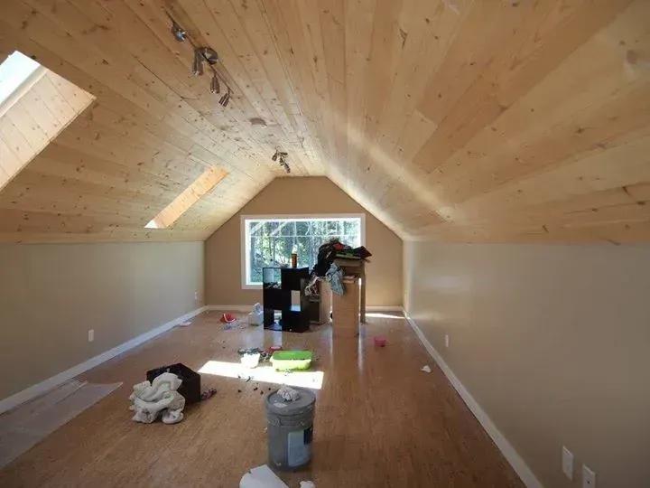 Attic room with wood ceiling and floor, beige walls, a window, and miscellaneous items on the floor.
