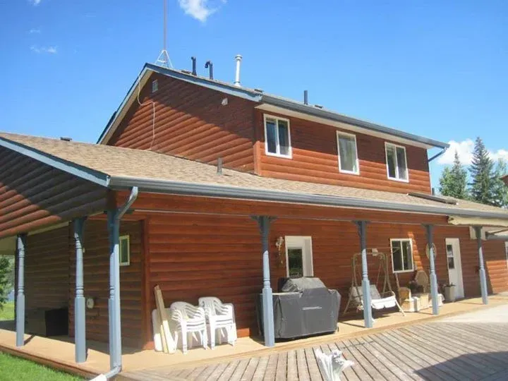 Two-story brown house with a covered porch. White windows, blue sky. Chairs and a grill on porch.