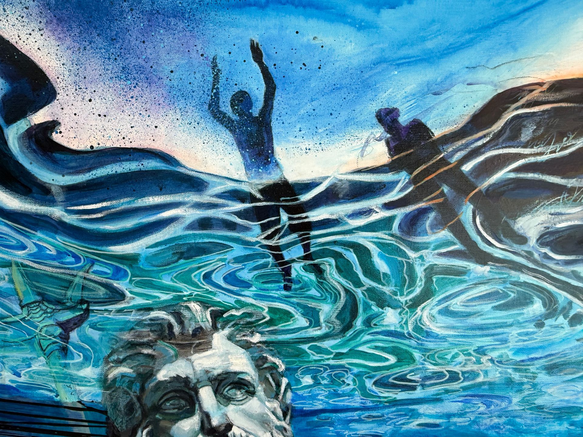 Person submerged in blue water, reaching upwards. Statue head submerged. Another figure on water's surface.