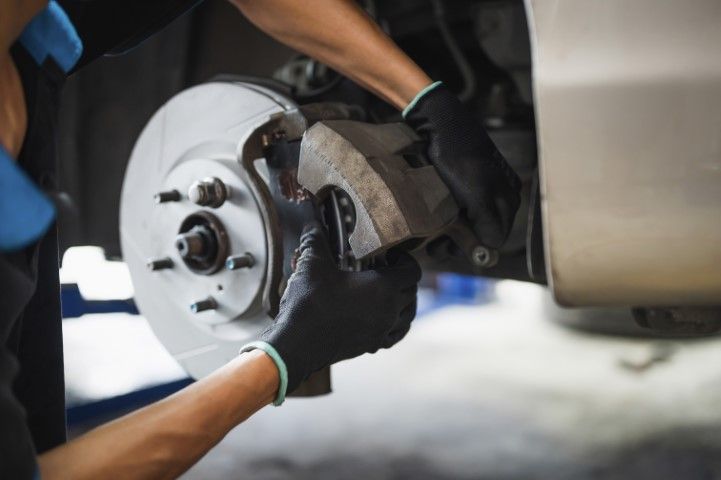 Hands wearing black gloves replacing brake pads on a car's rotor.