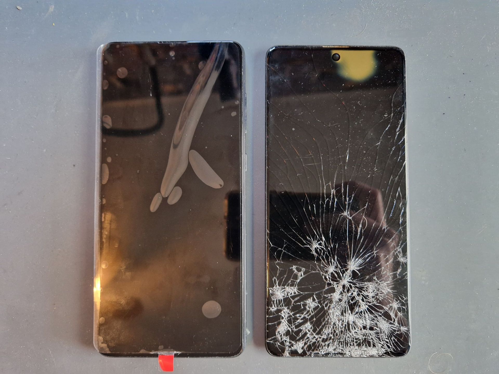 Een nieuw smartphonescherm naast een scherm met een gebroken display, beide naast elkaar op een grijze ondergrond.