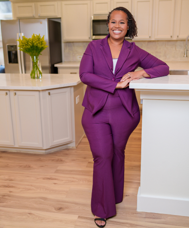 Woman in colorful patterned top smiles, holding a champagne flute, indoors near stairs.