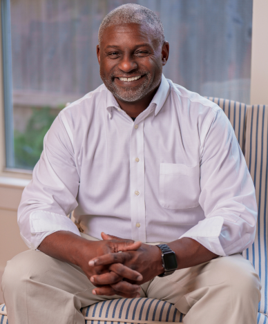 Man with gray hair in navy shirt, arms crossed, smiling slightly, indoors.