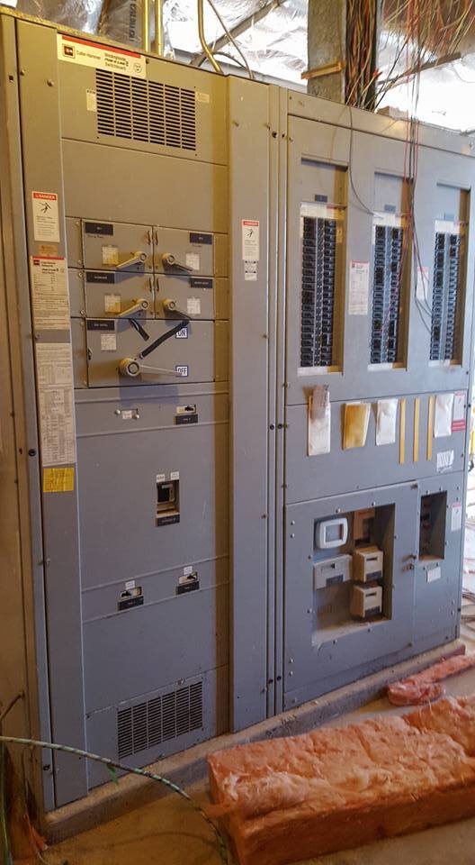 A large, grey industrial electrical switchgear cabinet with various circuit breakers and panels, located indoors.