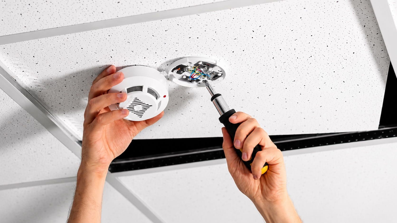 Electrician inspecting smoke detector wiring during a commercial inspection