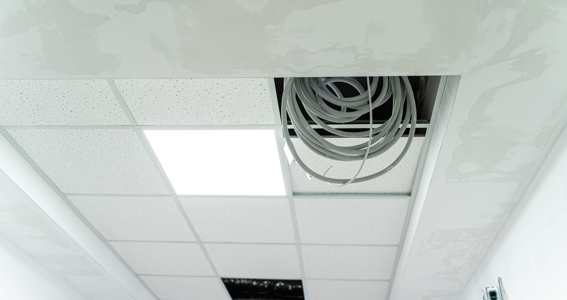 Electrician accessing ceiling wiring during a commercial lighting repair