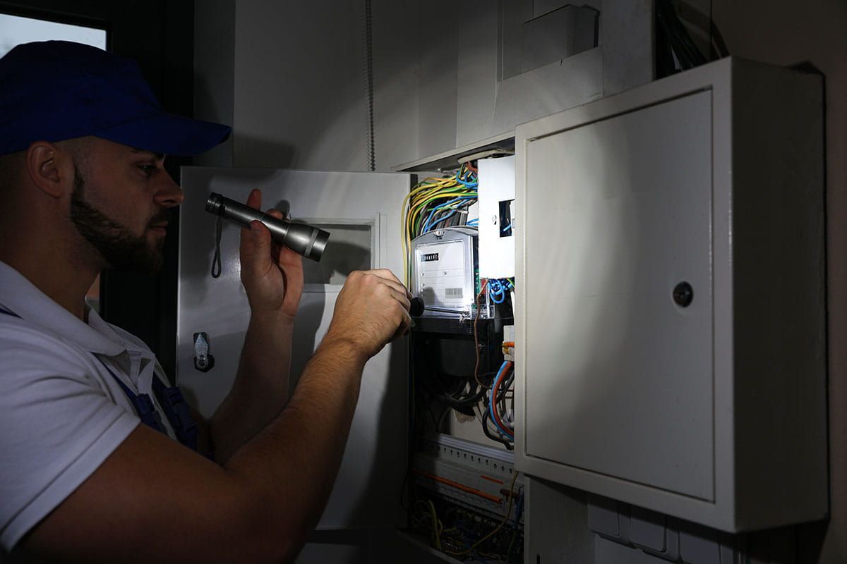 Electrician using a flashlight to inspect a home electrical meter panel