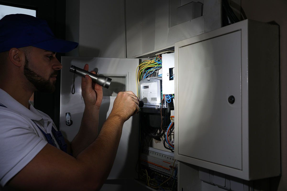 Electrician inspecting home breaker panel with flashlight