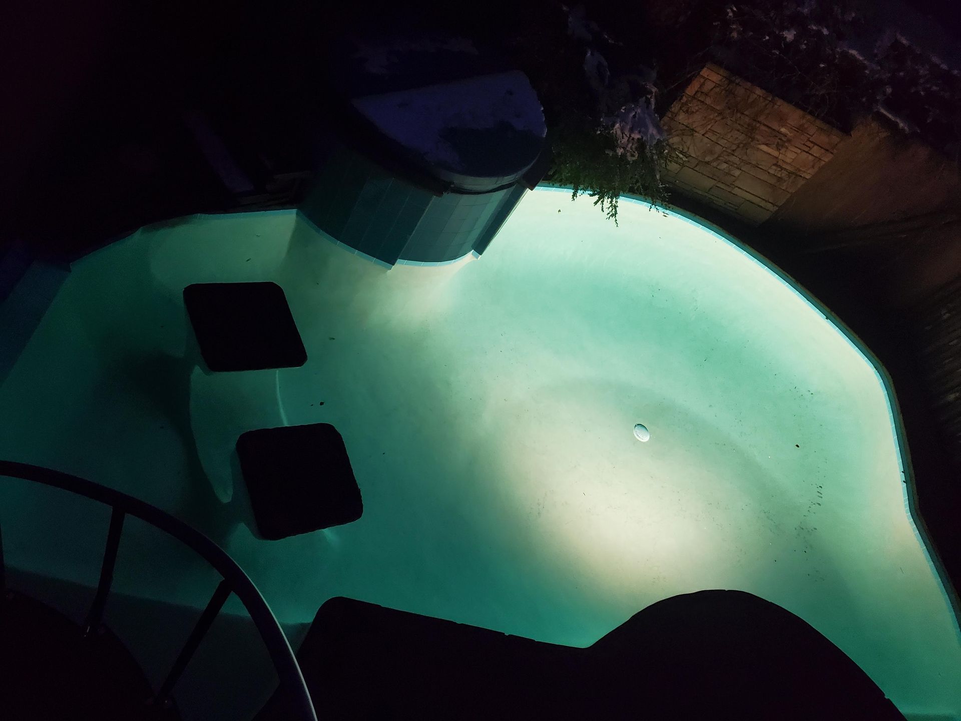 A Swimming Pool is Lit Up at Night With a Steering Wheel in the Foreground