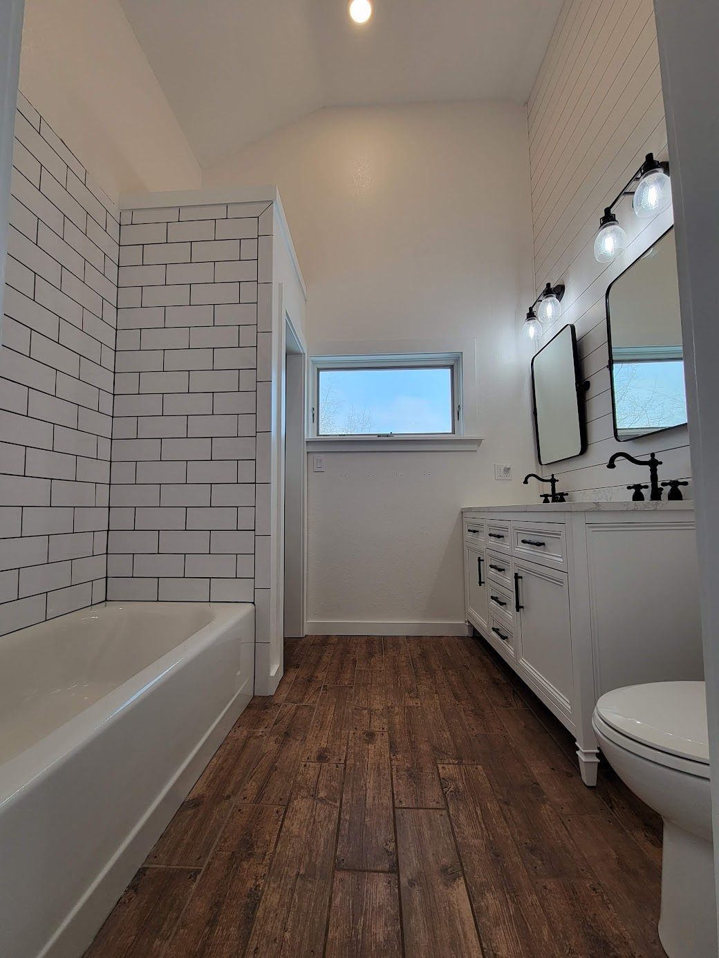 Bright bathroom with white subway tile, double sink vanity, bathtub, and wood-look flooring