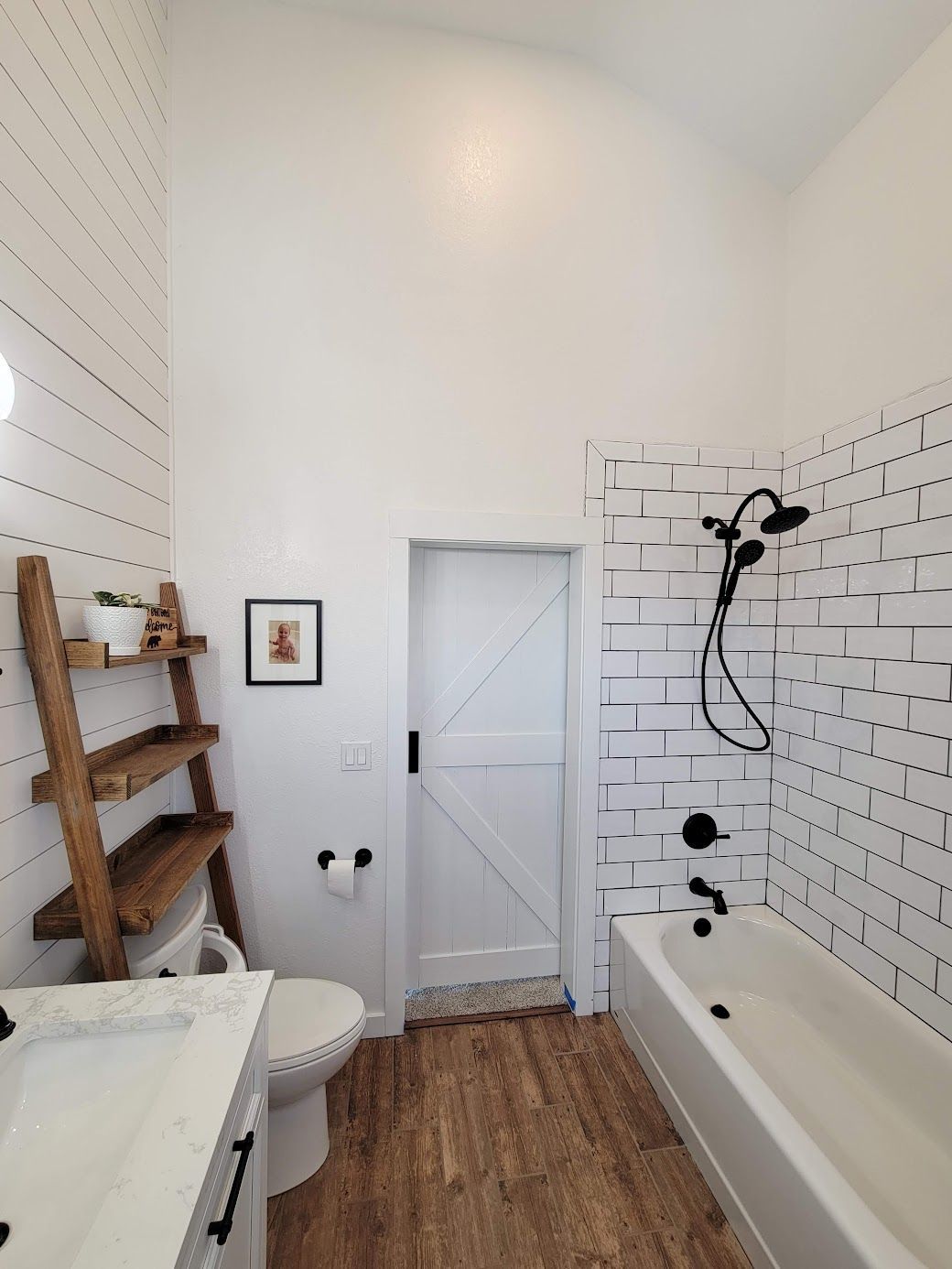 Small bright bathroom with white subway tile, wood floor, bathtub, toilet, and rustic shelf ladder.