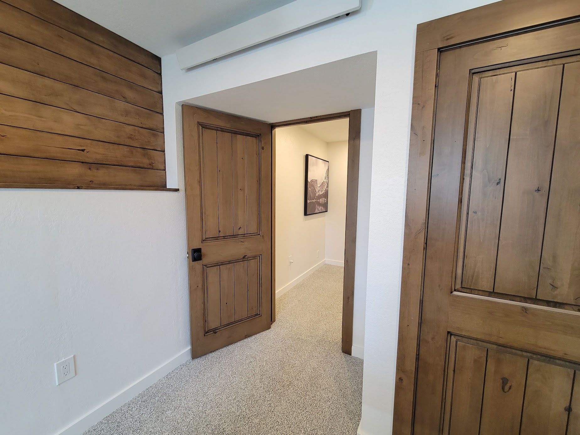 Interior hallway with white walls, wood trim, and an open wooden door leading to a carpeted room.