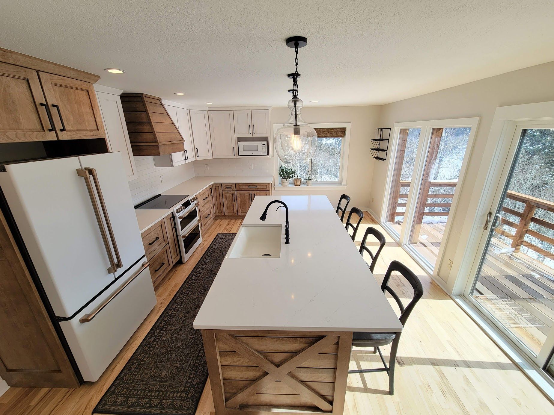 Bright modern kitchen with island, white cabinets, wood accents, and large windows looking out to a deck