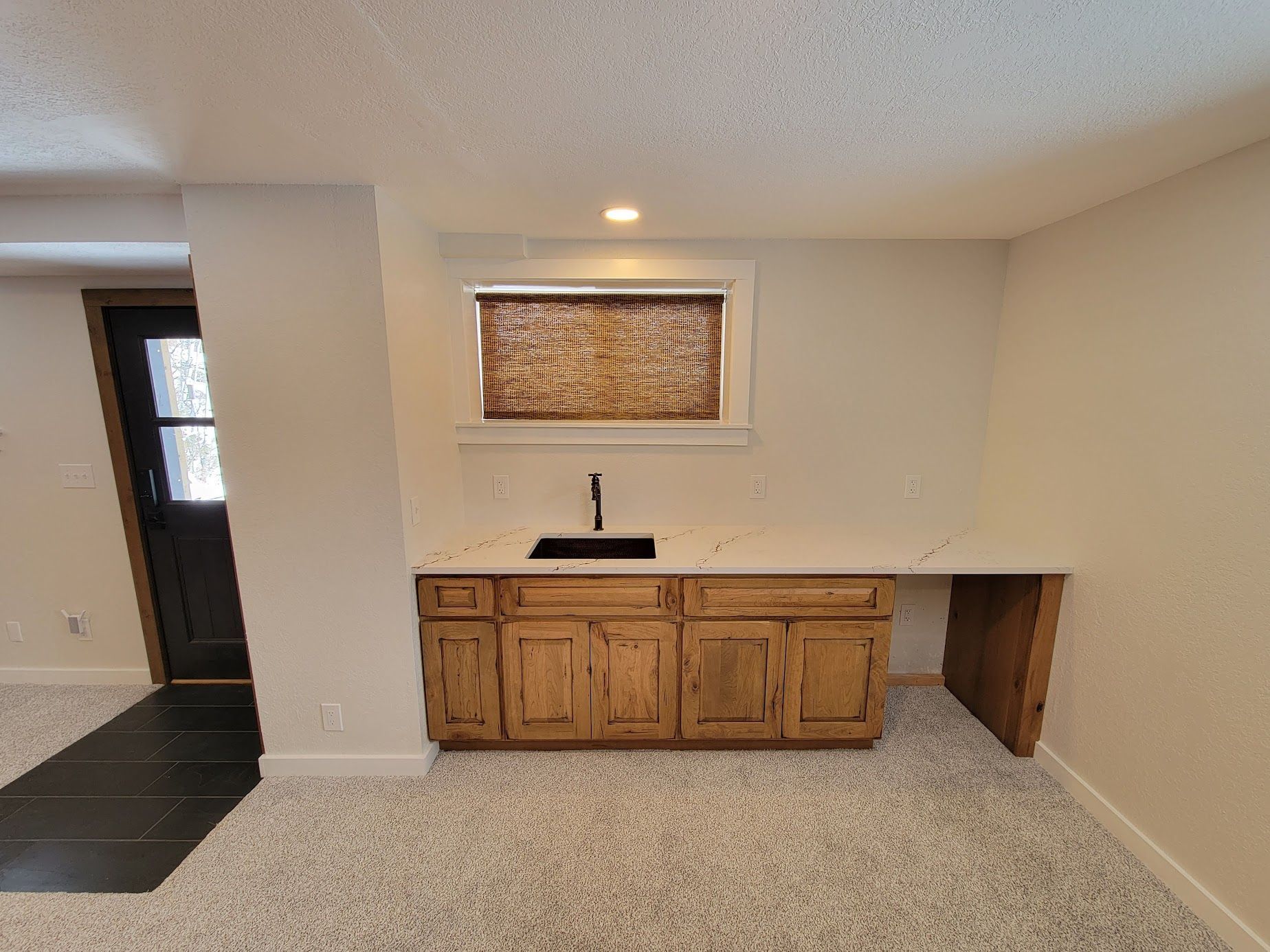 Small kitchen nook with wood cabinets, sink, and window shade in a carpeted room