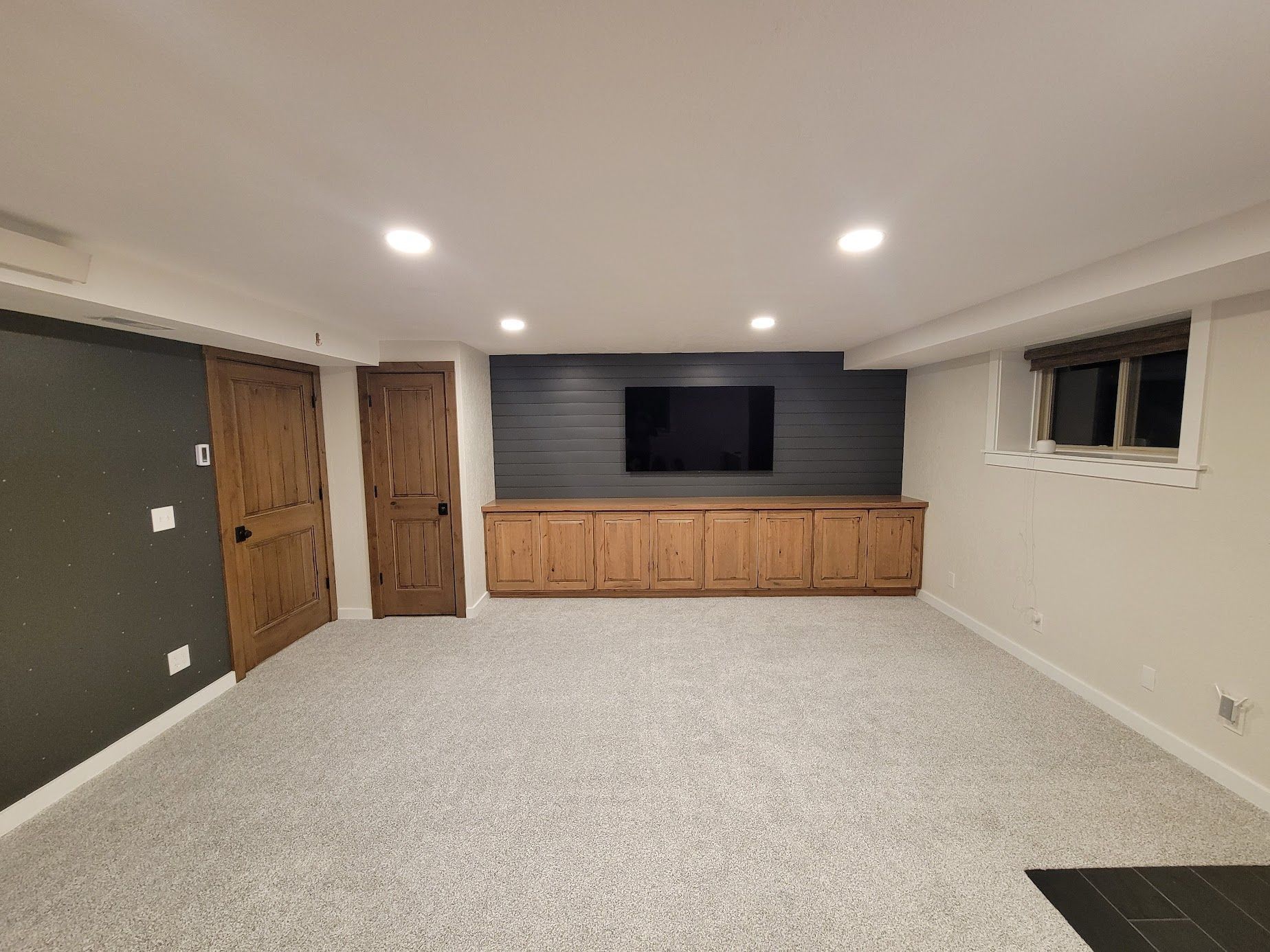 Spacious finished basement with gray carpet, wood cabinets, wall-mounted TV, and recessed lighting