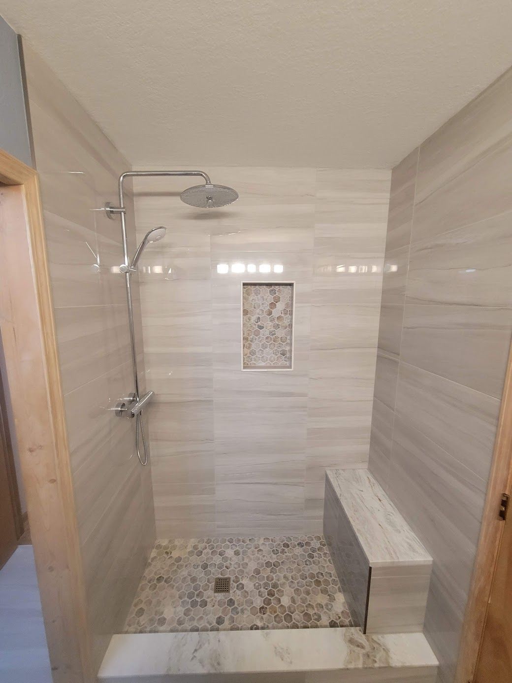 Modern tiled walk-in shower with stone floor, built-in bench, and rainfall showerhead