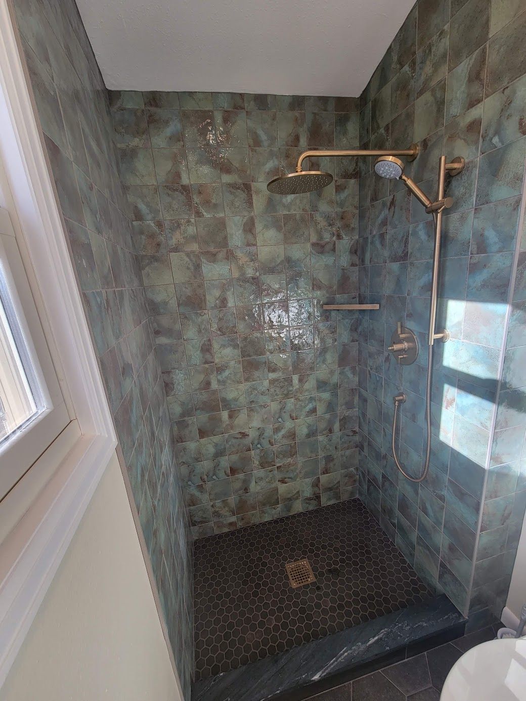 Small tiled shower stall with green marble walls, black floor, and a window on the left.