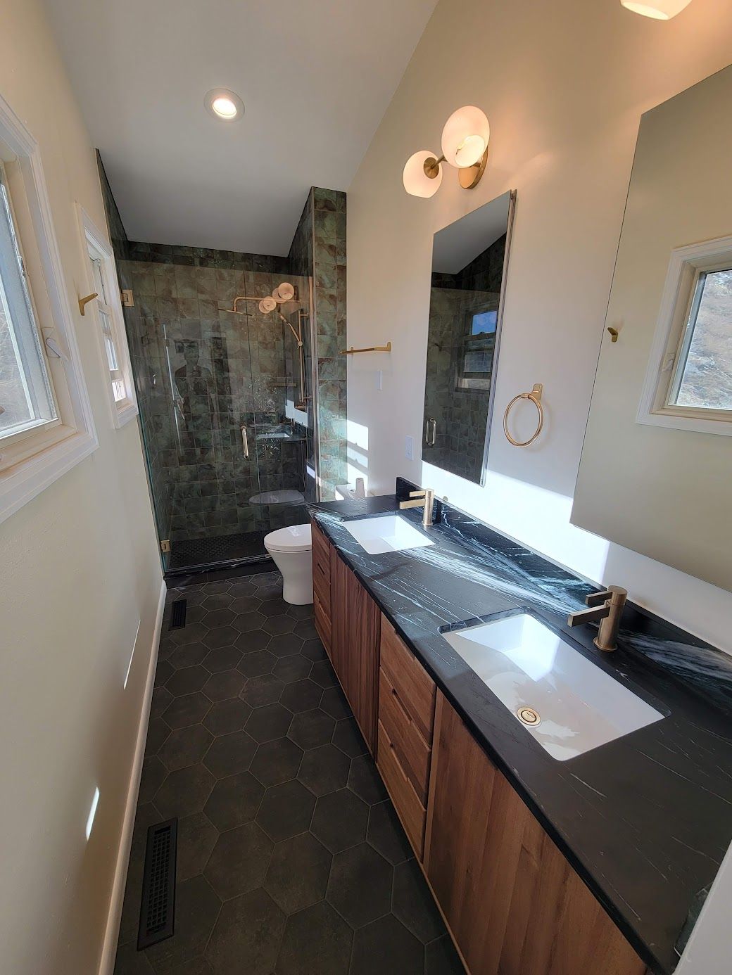 Narrow bathroom with dark vanity, white sink, large mirror, and tiled shower at the far end.