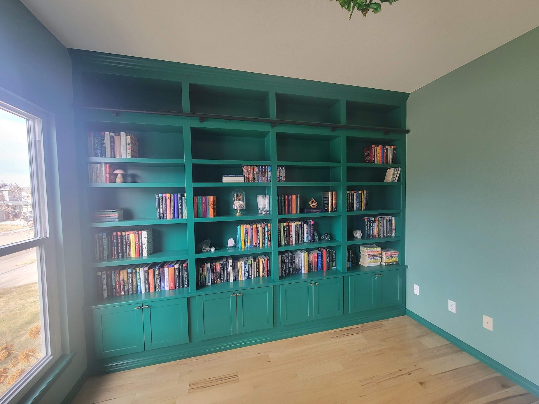 Teal built-in bookshelves filled with books in a sunlit room with hardwood floors and a window.